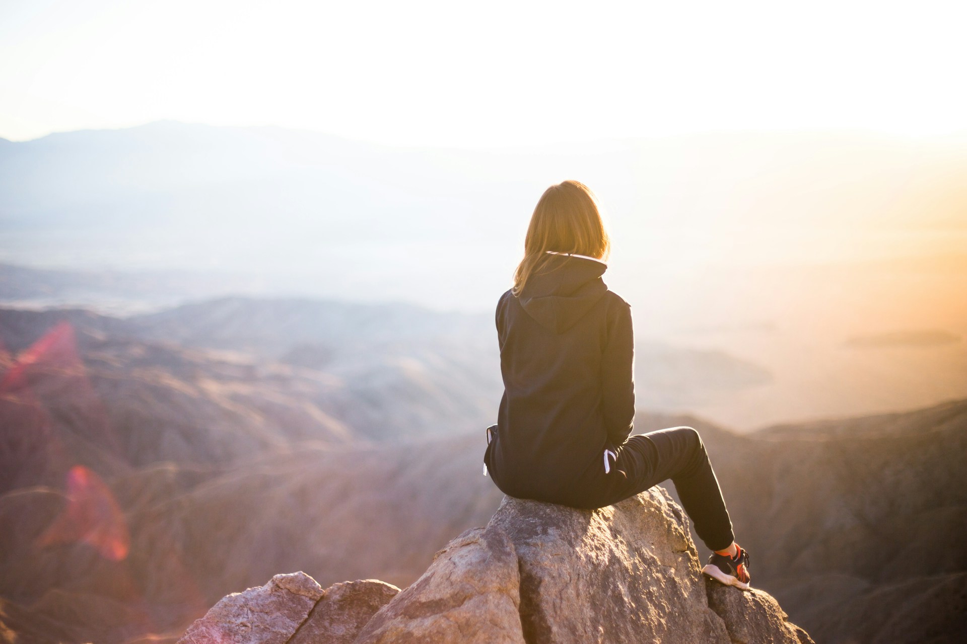 Woman sitting on top of mountain, looking at the landscape